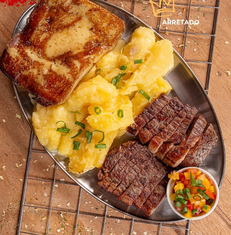 Prato Arretado: carne de sol fatiada, mandioca gratinada com queijo e queijo coalho grelhado, em travessa de metal.