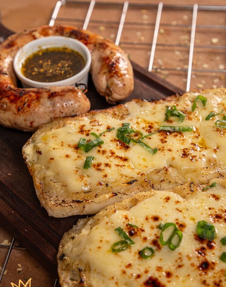 Chori & Pan: pão de alho gratinado em ciabatta ao lado de linguiça artesanal grelhada e molho de ervas.